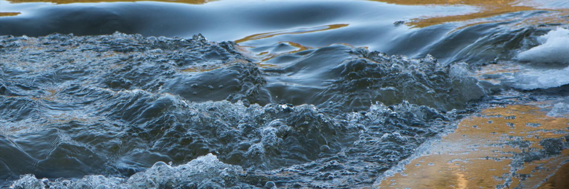Rushing water over a small waterfall with reflections.